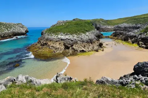 Una cala asturiana con aguas turquesas y arena dorada, rodeada de acantilados verdes. Un paraíso entre las playas más bonitas de Asturias.
