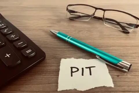 Kalkulator, zielony długopis i okulary leżą obok kartki z napisem PIT. Czas rozliczyć PIT 36L.