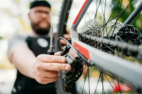 Mężczyzna z brodą dokręca śruby w przerzutce rowerowej. Dbałość o detale podczas tych momentów dokręcania śrub w rowerze zapewnia płynną jazdę.
