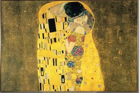 Gustav Klimts "Der Kuss" zeigt ein goldenes Paar, das sich innig umarmt und küsst, umgeben von einem abstrakten, funkelnden Hintergrund.