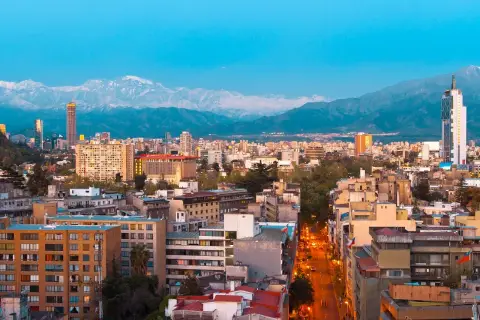 Widok na Santiago, stolicę Chile, z górami w tle. Miasto tętni życiem, a światła uliczne rozświetlają wieczór.
