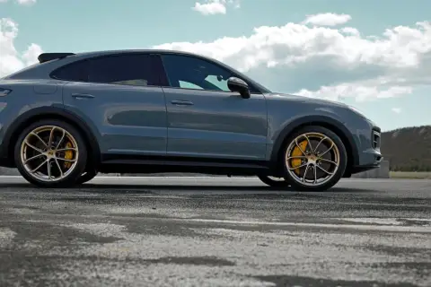 Szary Porsche Cayenne Turbo GT z żółtymi zaciskami hamulcowymi na złotych felgach, zaparkowany na pustej drodze z górzystym krajobrazem w tle.