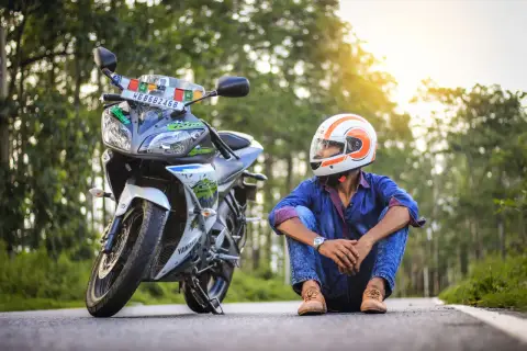 Giovane con casco arancione e bianco, seduto accanto alla sua moto. Spera di allargare il casco stretto per un viaggio più comodo.