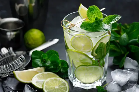 Szklanka orzeźwiającego mojito z limonką i miętą, otoczona lodem i składnikami.