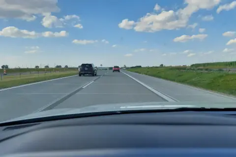 Widok z samochodu na autostradzie. Widać inne pojazdy i znaki ograniczające prędkość do 80 km/h.