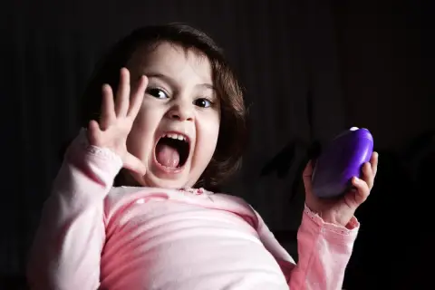 Niña con expresión de miedo, gritando y levantando una mano. Sostiene un objeto morado. Representa el miedo en niños de 6 a 12 años.