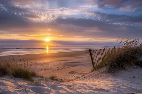 Coucher de soleil sur la plage de l'Île d'Oléron, avec des dunes de sable, des herbes folles et un ciel aux couleurs chaudes.