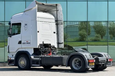Biała Scania R420 z logo "Erik Hoek Transport" stoi przed nowoczesnym budynkiem z zielonymi oknami.