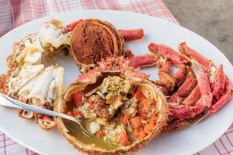 Centollo marisco preparado en una fuente blanca, con su coral y patas rojas. Una cuchara sirve el interior jugoso.