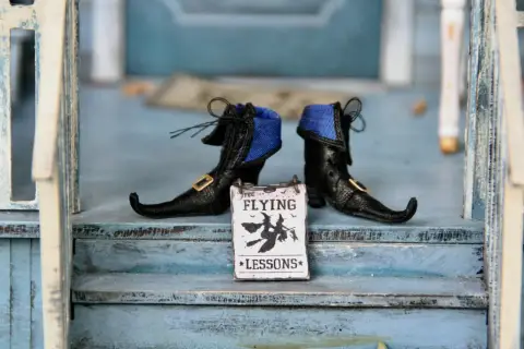 Stivaletti da strega neri con un cartello "Free Flying Lessons" per le parole di Halloween.