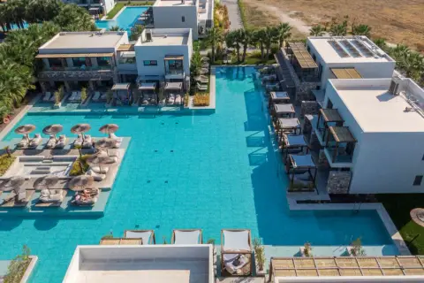 Luksusowy resort z basenami i leżakami przy plaży Caravia Beach Kos. Palmy i nowoczesna architektura tworzą idealne miejsce na relaks.