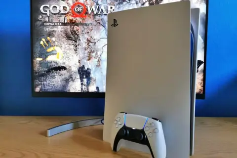 Konsola PlayStation 5 z kontrolerem DualSense obok. Na ekranie widoczny tytuł gry "God of War" i opcje "Nowa gra", "Ustawienia". Idealny moment na playstation aktualizacja.