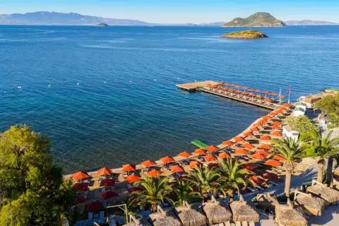 Piękna plaża z rzędem pomarańczowych parasoli i leżaków, drewniany pomost, palmy i turkusowe morze. Idealne miejsce na wakacje, zgodnie z kadikale resort opinie.