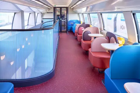 Wnętrze pociągu TGV inOui z kolorowymi siedzeniami i stolikami.