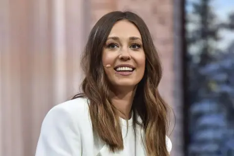 Izabella Krzan w białej marynarce, uśmiechnięta, z mikroportem przy uchu.