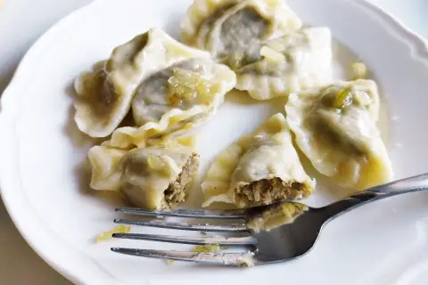 Pyszne pierogi z soczewicą na białym talerzu, jeden nadgryziony, obok widelec.