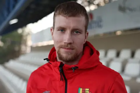 Młody piłkarz w czerwonej bluzie z herbem Korony Kielce, gotowy na nowe transfery.
