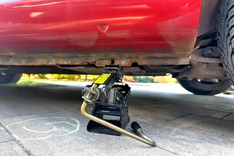Podnośnik samochodowy pod czerwonym autem, gotowy do akcji. Dowiedz się, jak podnieść auto lewarkiem, by wymienić koło.