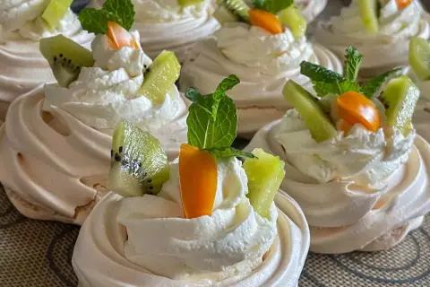 Pyszne gniazdka bezowe z kremem mascarpone, ozdobione kawałkami kiwi, pomarańczy i listkami mięty.