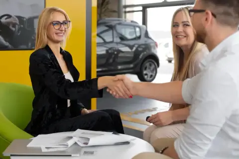 Uśmiechnięta para zawiera umowę cesji leasingu z doradcą w salonie samochodowym.
