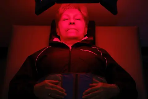 Mujer relajada bajo luz roja, experimentando los beneficios de la terapia de luz para el bienestar.