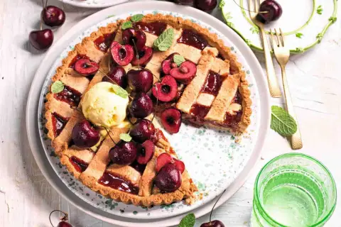 Una deliziosa crostata di ciliegie, guarnita con ciliegie fresche, gelato alla vaniglia e foglioline di menta. Perfetta per un dolce estivo.