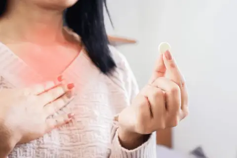 Kobieta z pieczeniem w klatce piersiowej trzyma tabletkę, zastanawiając się: ipp co to za lek?