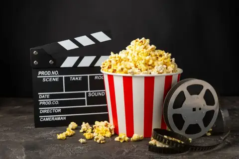 Klapka filmowa, kubełek popcornu i rolka taśmy filmowej na ciemnym tle.