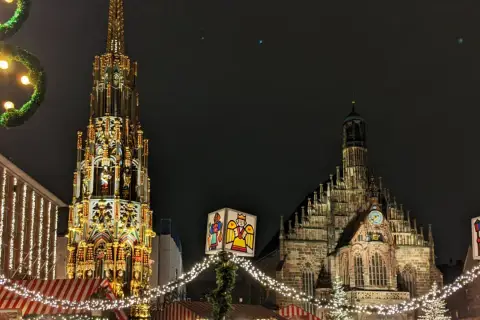 Nocne jarmarki bożonarodzeniowe w Europie. Wspaniała iluminacja zabytkowej fontanny i kościoła, ozdobione świątecznymi lampkami i dekoracjami.