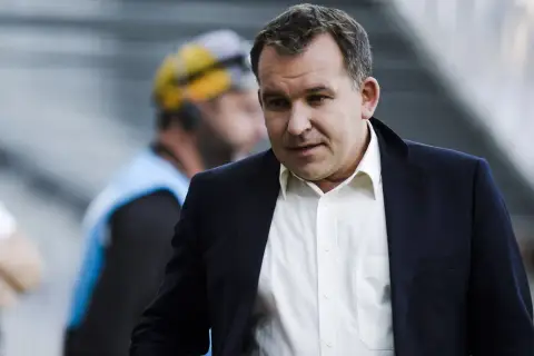 Żyżyński dziennikarz sportowy w garniturze, z uwagą obserwuje wydarzenia na boisku.