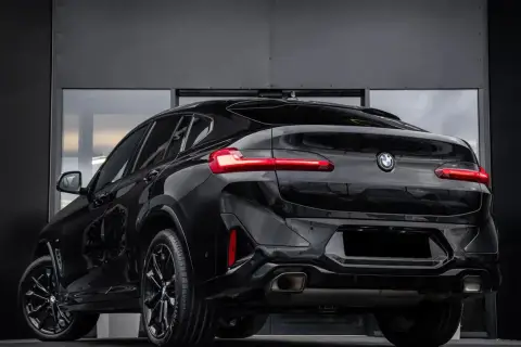 Elegancki, czarny BMW X4 G02 z przyciemnianymi szybami i sportowymi felgami prezentuje się imponująco na tle nowoczesnej, szarej ściany.