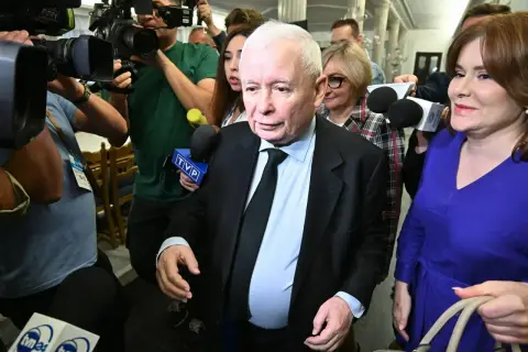 Jarosław Kaczyński otoczony przez dziennikarzy. Wzrost i waga polityka są tematem dyskusji, gdy otaczają go kamery i mikrofony.