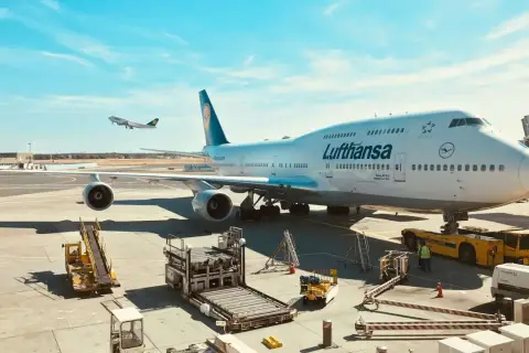 Lufthansa bagaż podręczny czeka na załadunek obok gigantycznego Boeinga 747-400 na lotnisku.