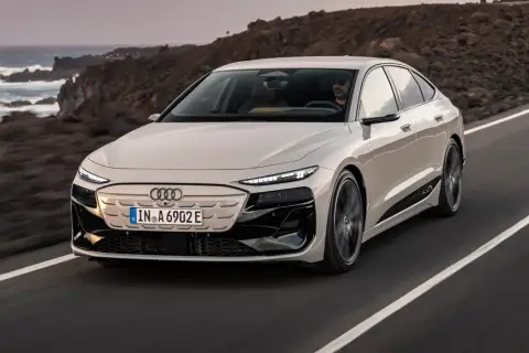 Elegancki Audi A6 e-tron w kolorze kremowym przemierza malowniczą, nadmorską drogę.