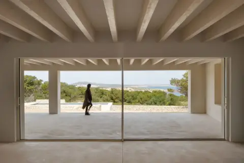 Persona camina por una terraza moderna con grandes ventanales que muestran varios tipos de ventanas correderas, vistas al mar y vegetación.