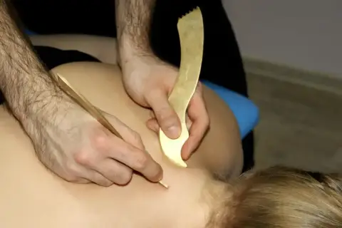 Masaż narzędziami do pinoterapii. Terapeuta pracuje nad karkiem pacjenta, używając złotych przyrządów do głębokiego masażu tkanek.
