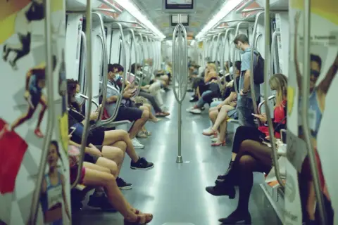 Interno di un vagone della metro di Roma, con passeggeri seduti e in piedi. Si vede come funziona la metro a Roma, con le barre di sostegno e i sedili bianchi.