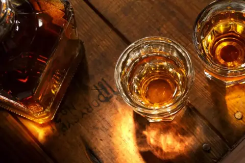 Butelka i dwa kieliszki bursztynowego trunku na drewnianym blacie. Zastanawiasz się, czym się różni koniak od whisky?