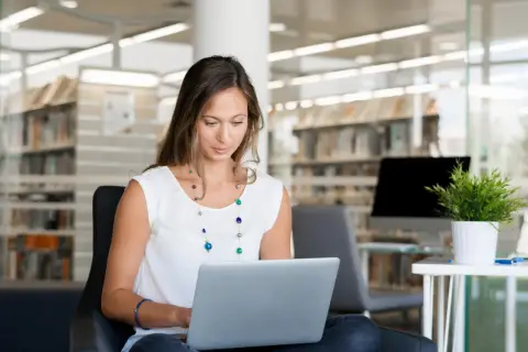 Kobieta siedzi w bibliotece, ucząc się, jak założyć PUE ZUS na laptopie.