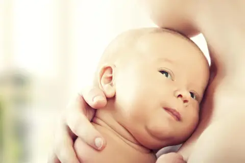 Noworodek wtulony w ramię dorosłego, z widoczną twarzą i uchem.