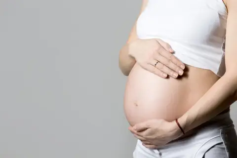Ciężarna kobieta trzyma dłonie na brzuchu. Temat: umowa na zastępstwo a ciąża.
