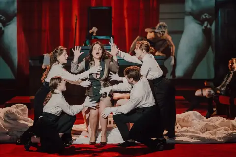 Kalisz teatr repertuar: scena z dramatycznym aktem, gdzie aktorka w centrum otoczona jest przez innych wykonawców.