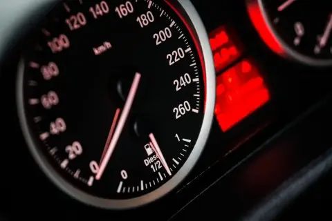 Zbliżenie na deskę rozdzielczą samochodu: prędkościomierz pokazuje 80 km/h, a obok wskaźnik paliwa wskazuje prawie pełny bak.
