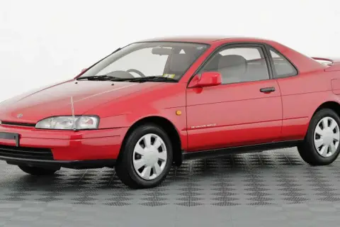 Czerwone, dwudrzwiowe Toyota Paseo z lat 90. na szarym, kratkowanym tle.