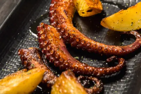 Tentacules de poulpe a la plancha, grillés à la perfection, servis avec des quartiers de pommes de terre dorées. Un délice croustillant et savoureux.