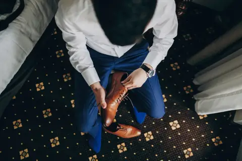 Mężczyzna w niebieskim garniturze i białej koszuli zakłada brązowe, eleganckie buty. Idealne pytanie: jakie buty do niebieskiego garnituru?