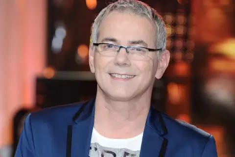 Robert Janowski ile ma lat? Uśmiechnięty mężczyzna w okularach, w granatowej marynarce i białej koszulce.