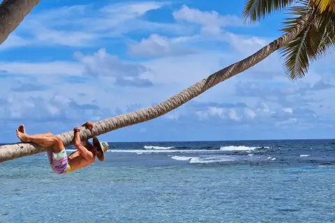 Mężczyzna w kapeluszu wisi na palmie nad turkusową wodą. Idealny dzień na plaży w Laguna Beach.