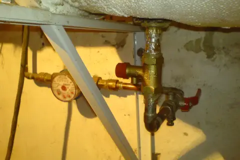 Instrukcja jak zamontować zawór bezpieczeństwa przy bojlerze. Widoczny wodomierz i instalacja wodna.