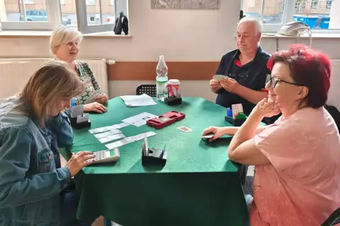 Cztery osoby grają w brydża dla początkujących przy zielonym stole.
